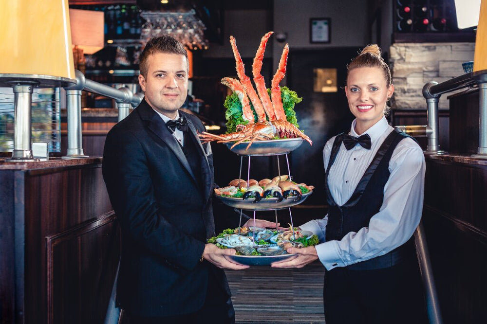 Man and woman displaying a three-tier seafood tower in restaurant.